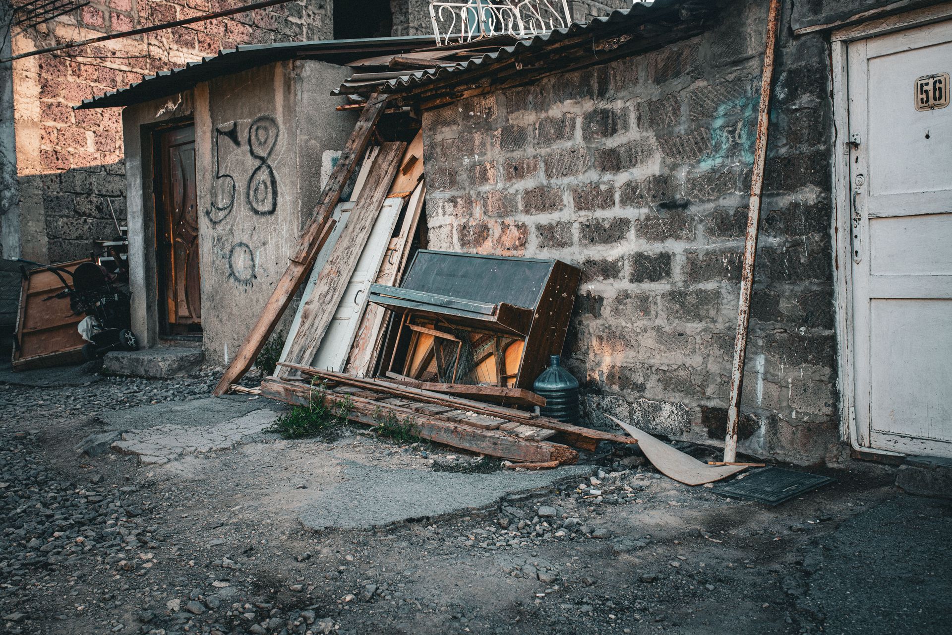 An old piano and debris in a rustic Armenian alleyway with textured walls.
